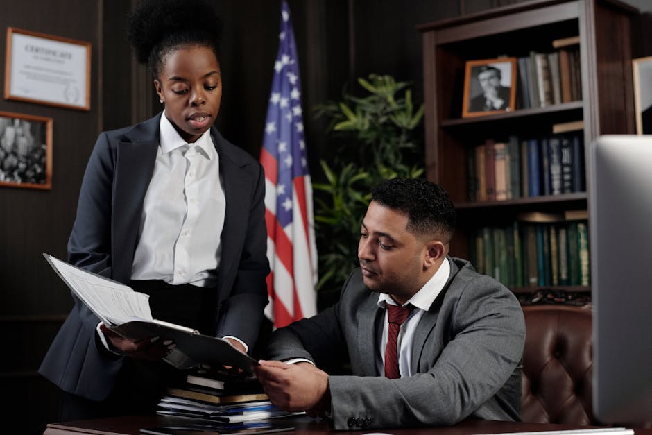 Two professionals discussing documents in an office setting with an American flag in the background.